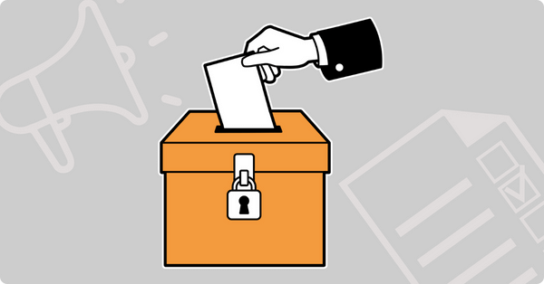 Eine Hand die einen Wahlzettel in eine orangene Wahlurne steckt.
